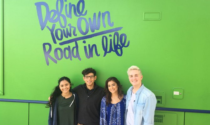 4 students in front of bright green tour bus that says define your own road in life