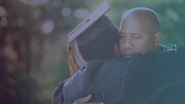 Father and son hugging, son wearing graduation cap