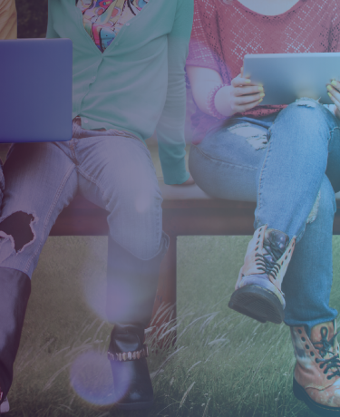 Teenagers on a bench outdoors using laptops and tablets