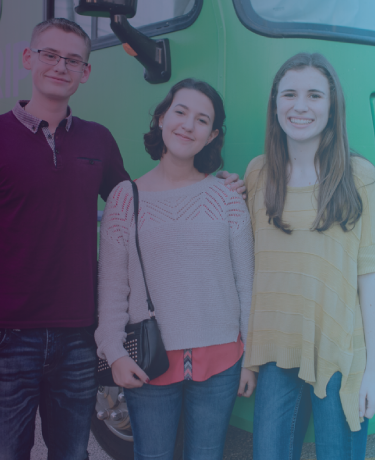 Three students standing in front of bright green Roadtrip Nation tour bus