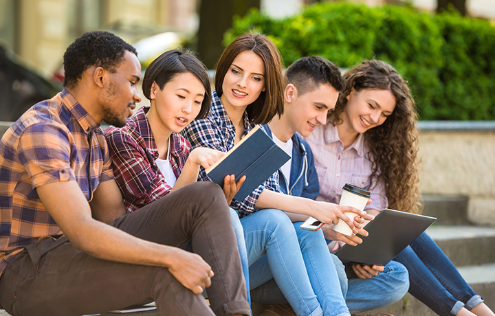 Un grupo de cinco adolescentes leyendo y trabajando juntos en un campus universitario