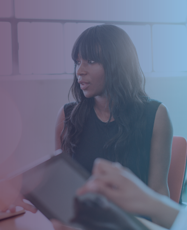 Black woman with long hair sitting at a table and speaking