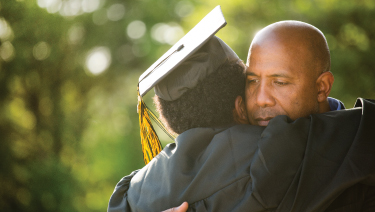 Male adult hugging student in grad cap